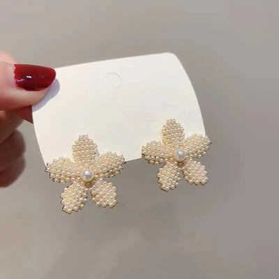 Flower-shaped earrings with pearls on a white card held by a hand with red nail polish.
