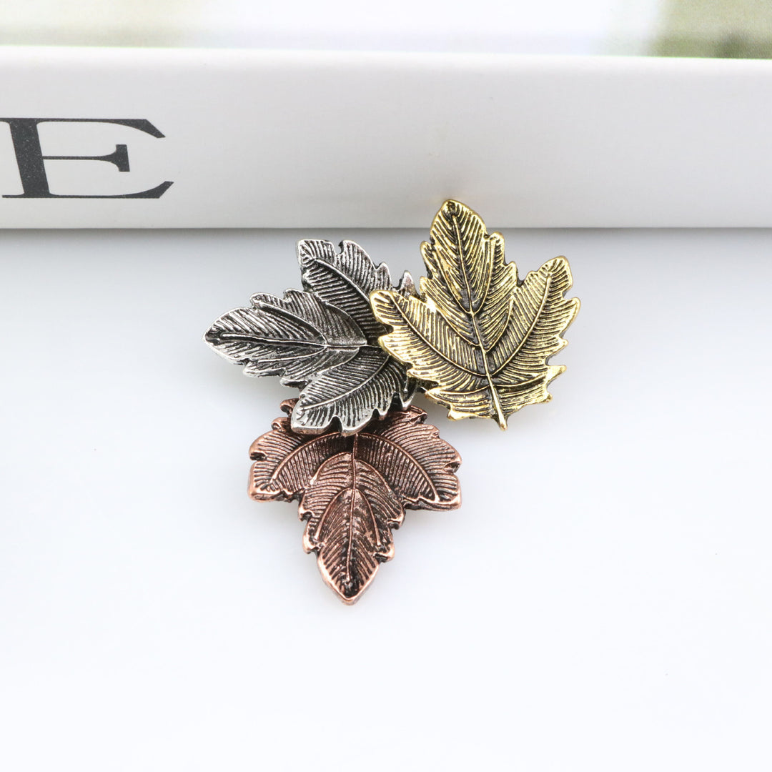 Three leaf-shaped pins in gold, silver, and bronze on a white surface.