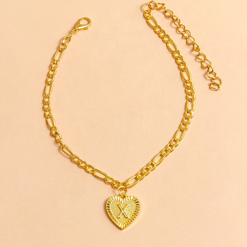 Gold chain bracelet with a heart-shaped pendant letter X on a beige background