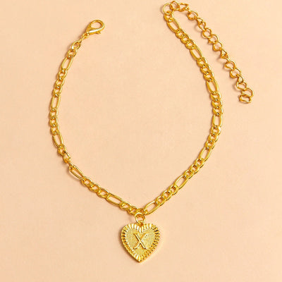 Gold chain bracelet with a heart-shaped pendant letter X on a beige background
