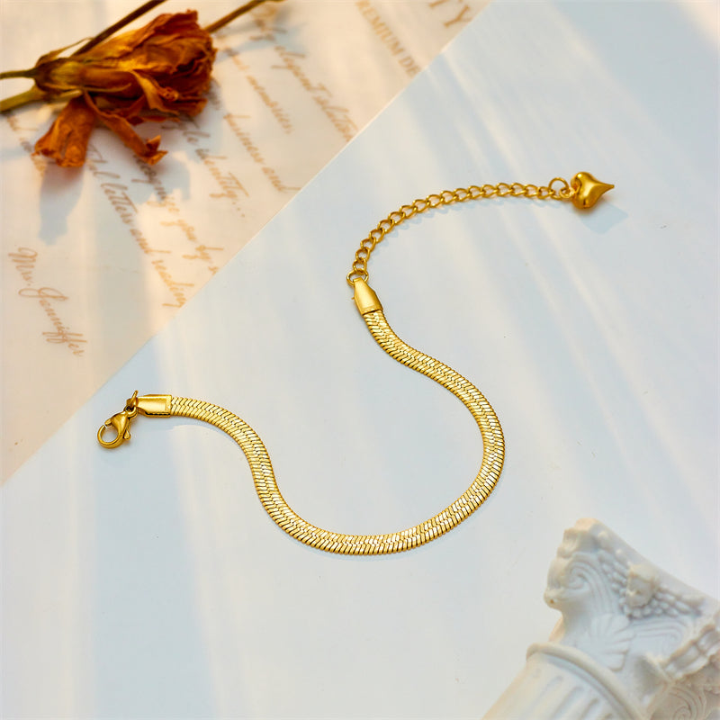 Gold bracelet on a textured surface with a decorative object and dried flower.