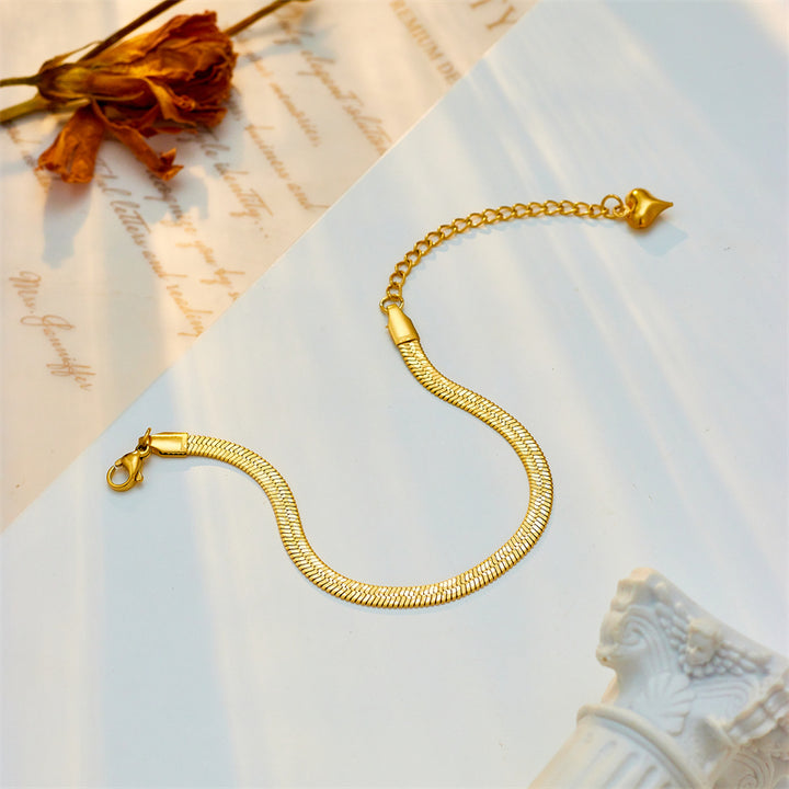 Gold bracelet on a textured surface with a decorative object and dried flower.