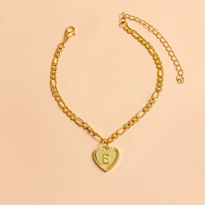 Gold chain bracelet with a heart-shaped charm letter E on a beige background