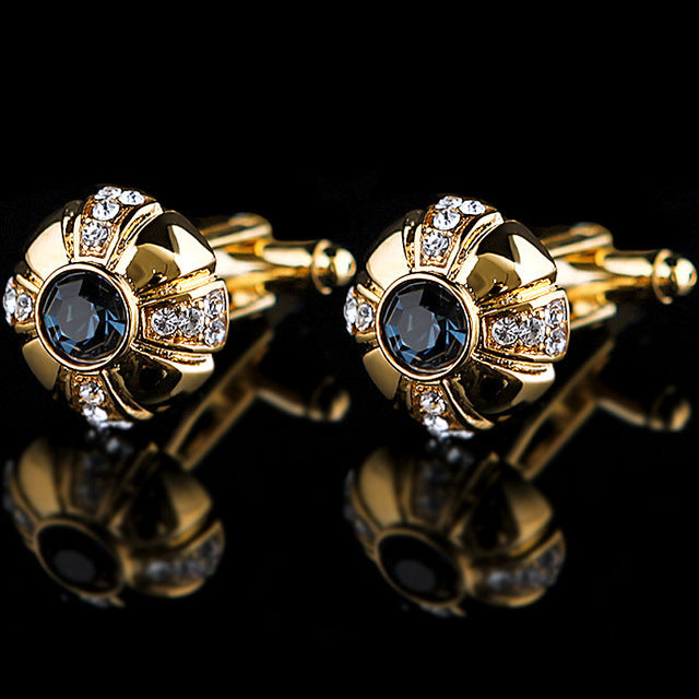 Gold cufflinks with blue gemstones and clear stones on a black background