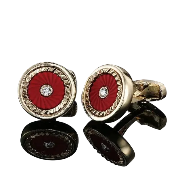 Gold cufflinks with red center and diamond-like stone on a reflective surface.