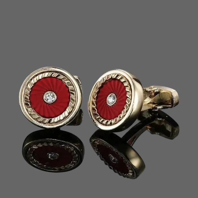 Gold cufflinks with red center and diamond-like stone on a gray background