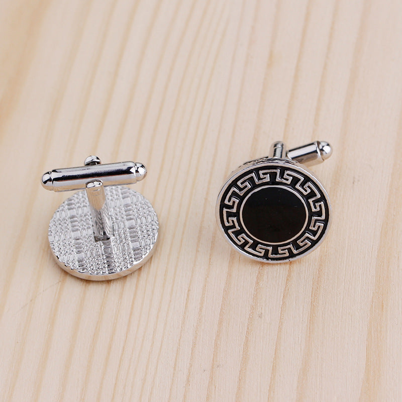 Two silver cufflinks with black center on a wooden surface