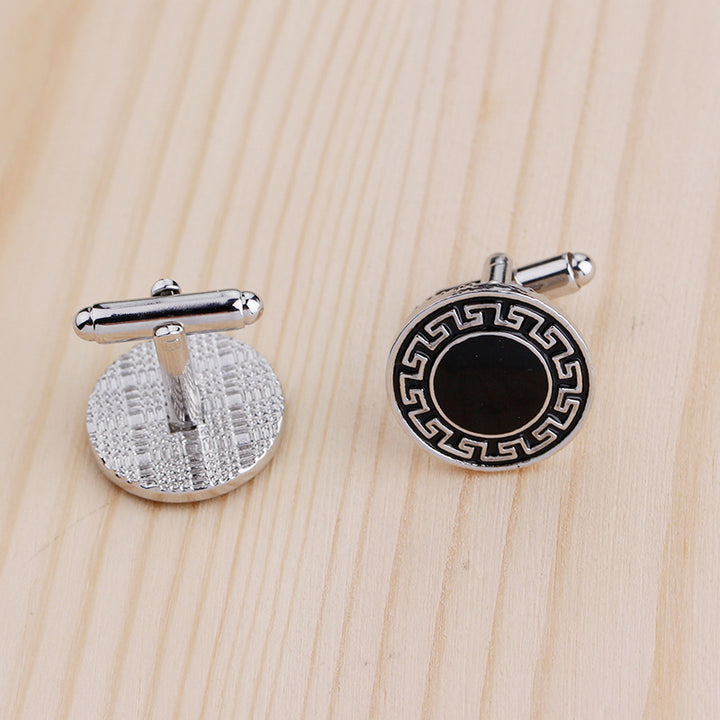 Two silver cufflinks with black center on a wooden surface