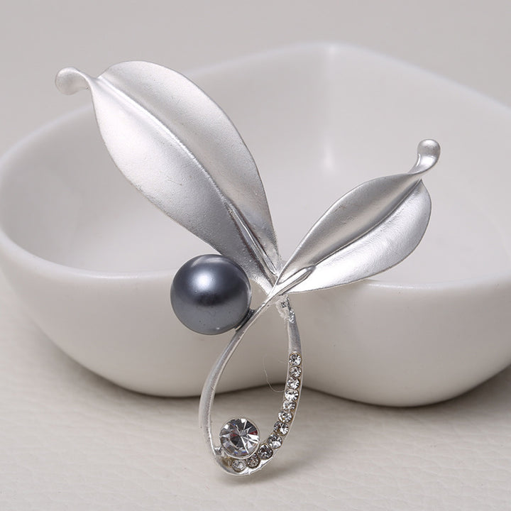 Silver brooch with a pearl and gemstone on a white background