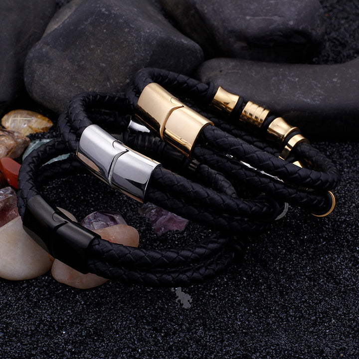 Black braided leather bracelet with gold and silver magnetic clasp on dark stone background