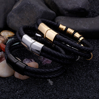 Black braided leather bracelet with gold and silver magnetic clasp on dark stone background