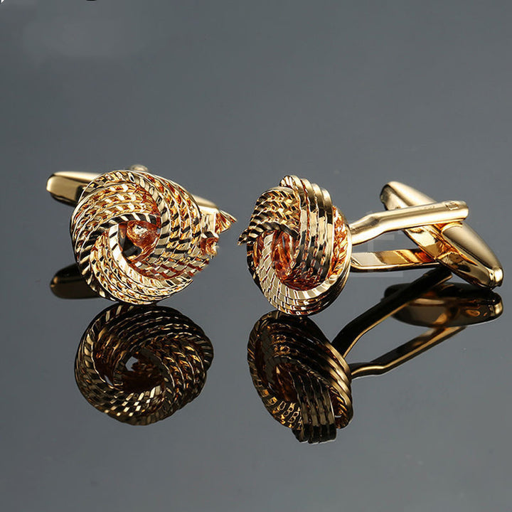 Pair of gold knot cufflinks on a reflective gray surface