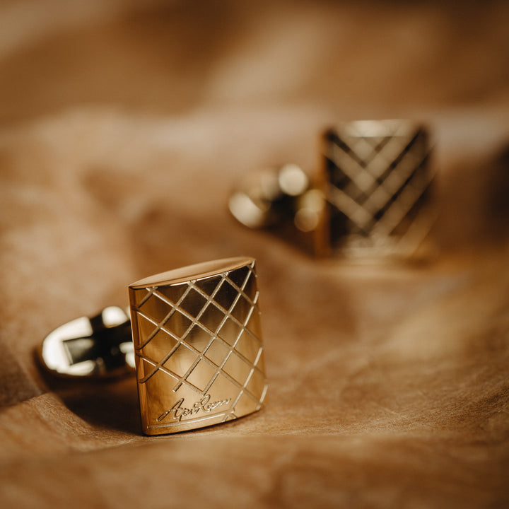 Gold cufflinks with a textured design on a brown leather surface