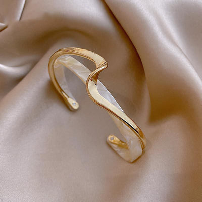 Gold and white cuff bracelet on a soft beige fabric background