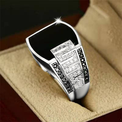 Silver ring with black and white gemstones on a beige cushion