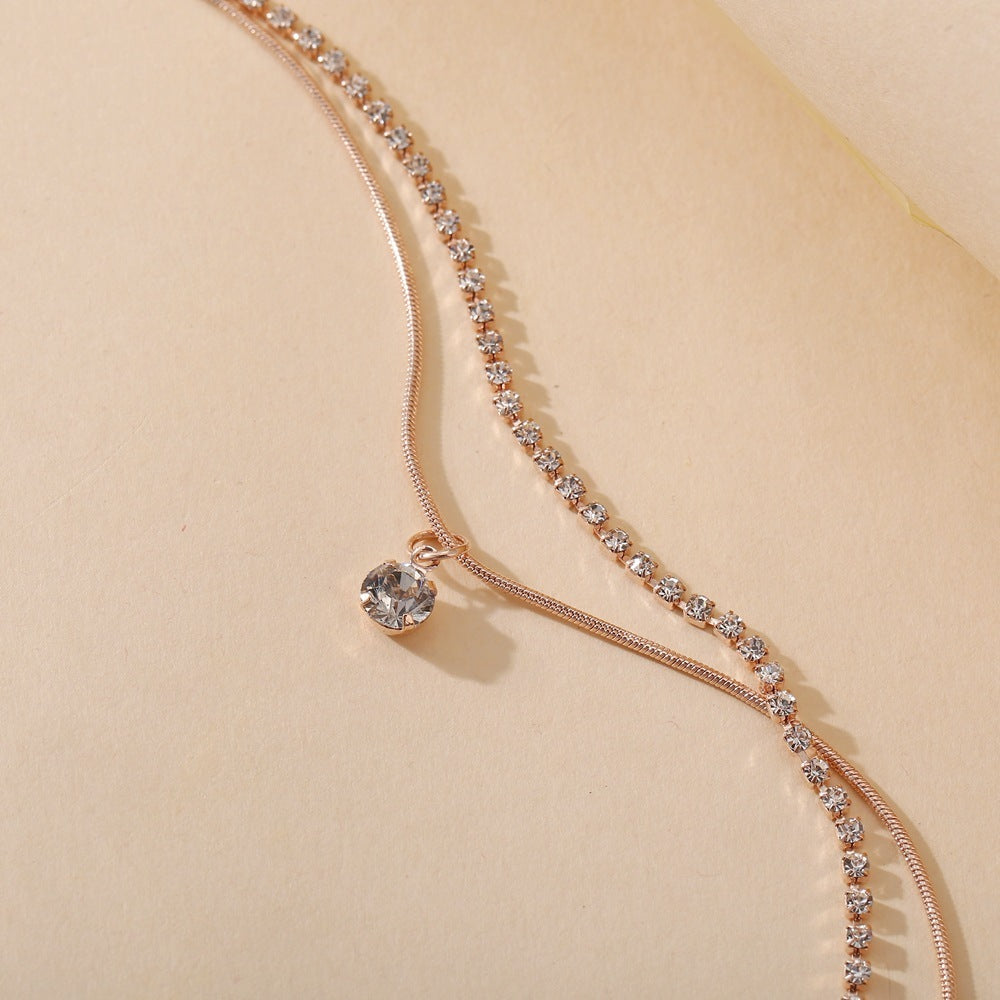 Rose gold anklet with clear gemstones on a beige background