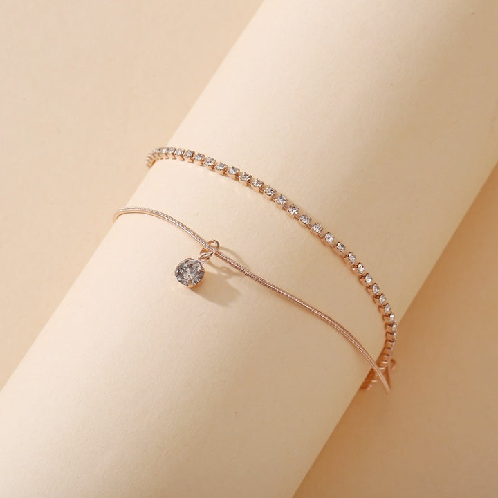 Rose gold anklets with clear gemstones on a beige background