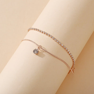 Rose gold anklets with clear gemstones on a beige background
