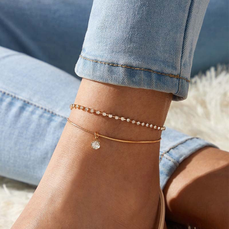 Close-up of a person's ankle with multiple gold anklets on a blurred background