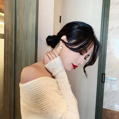 Woman wearing a beige off-shoulder sweater in a room with wooden walls.
