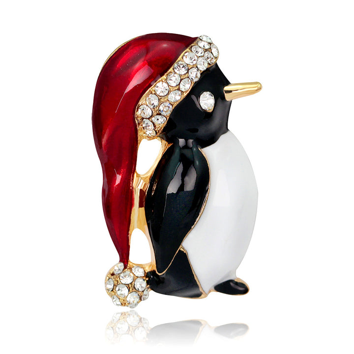 Penguin brooch with red hat and gold accents on a white background