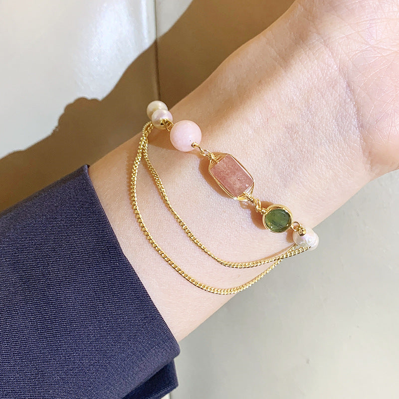 Gold bracelet with gemstones on a wrist against a neutral background