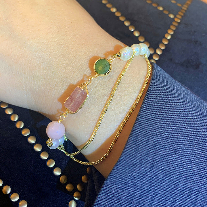 Gold bracelet with colorful beads on a wrist against a blue fabric background