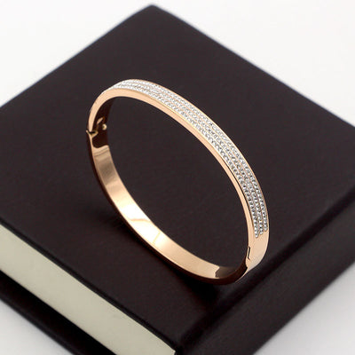 Rose gold bracelet with diamond accents on a black surface