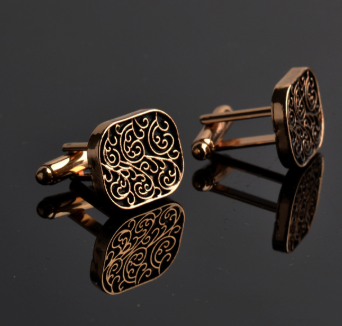 Gold cufflinks with intricate design on a reflective black surface