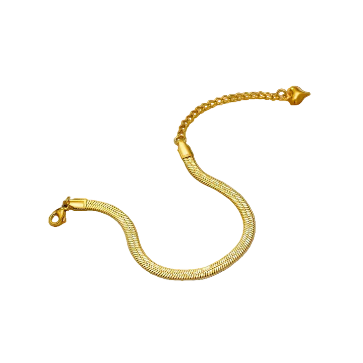 Gold bracelet on a textured surface with a decorative object and dried flower.