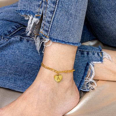 Gold anklet with a heart charm on a person's ankle wearing denim jeans.