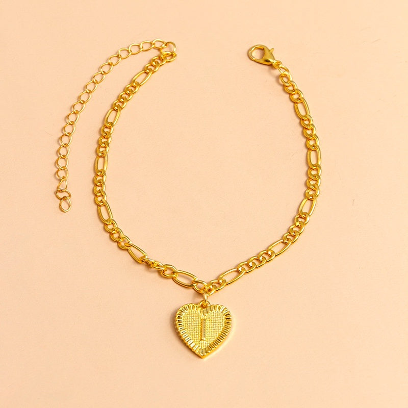 Gold chain bracelet with a heart-shaped pendant letter I on a peach background