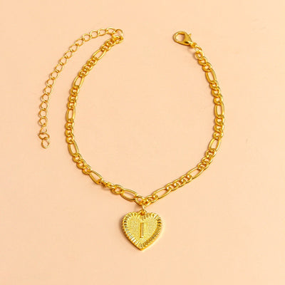 Gold chain bracelet with a heart-shaped pendant letter I on a peach background