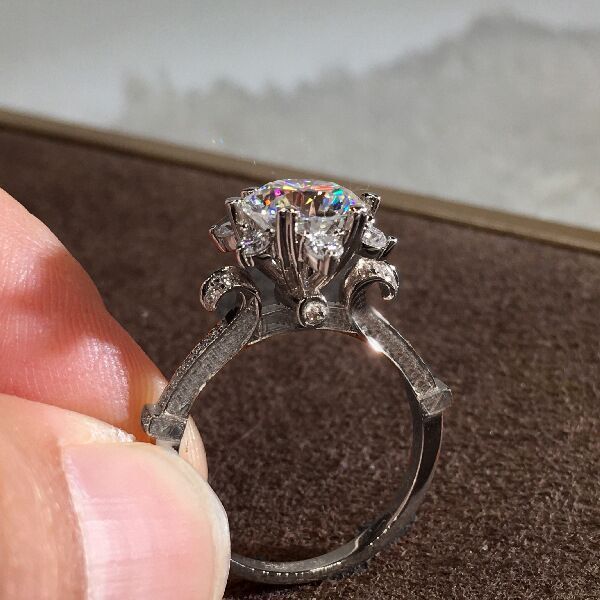 Silver ring with a large diamond held between fingers on a textured surface.