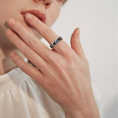 Close-up of a hand wearing a silver ring with moon phases on a neutral background