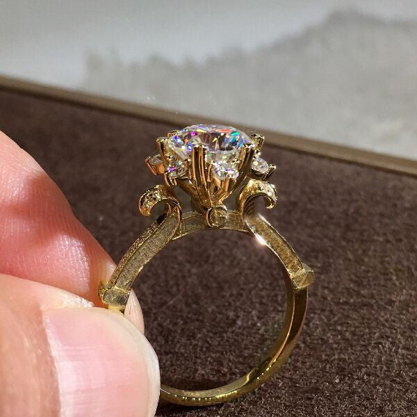 Gold ring with a large diamond held by a hand on a brown surface.