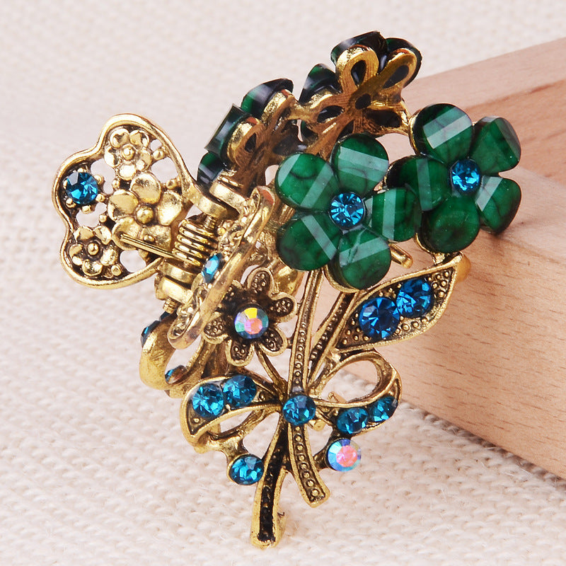 Decorative hair clip with green gemstones and gold accents on a textured surface