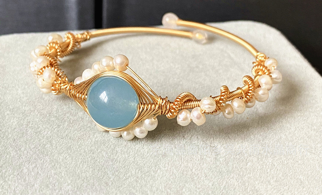 closeup view of Gold bracelet with pearls and a blue stone on a light gray surface