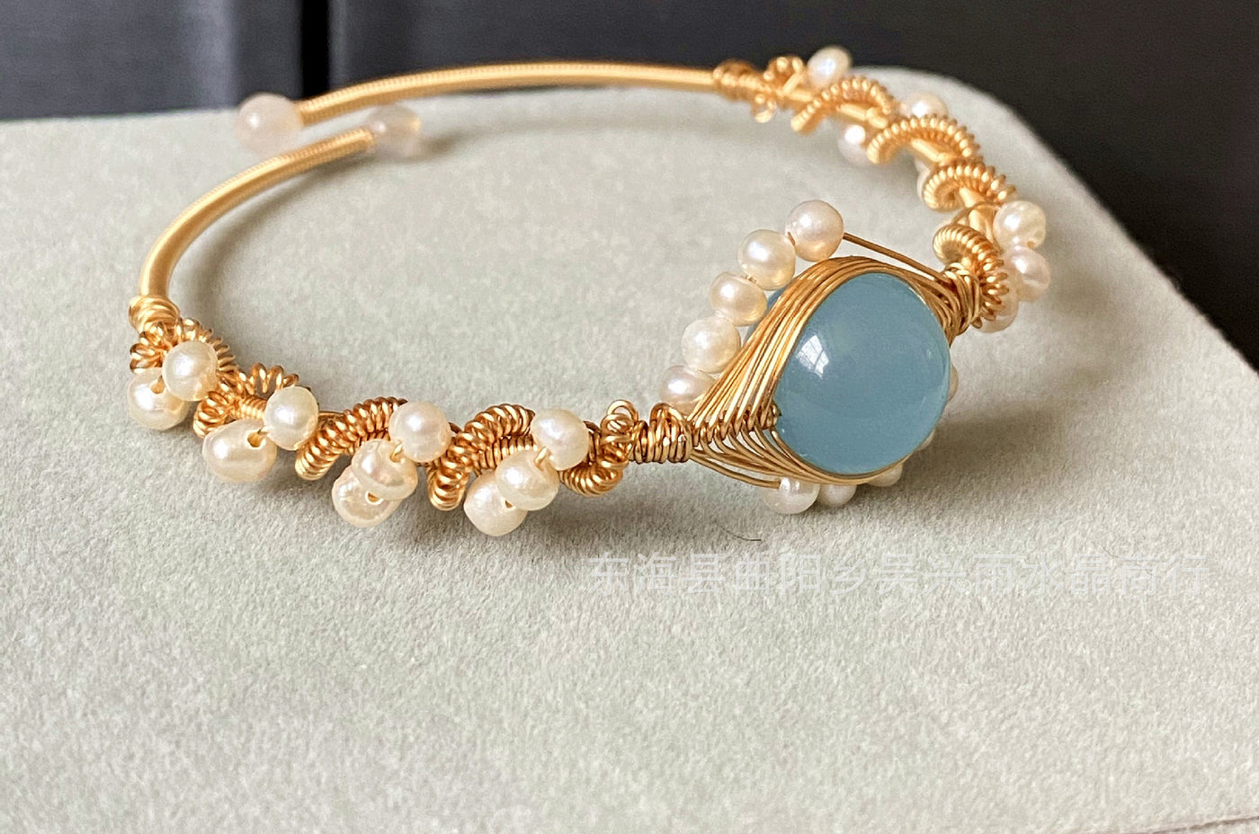 left side view of a Gold bracelet with pearls and a blue stone on a light gray surface