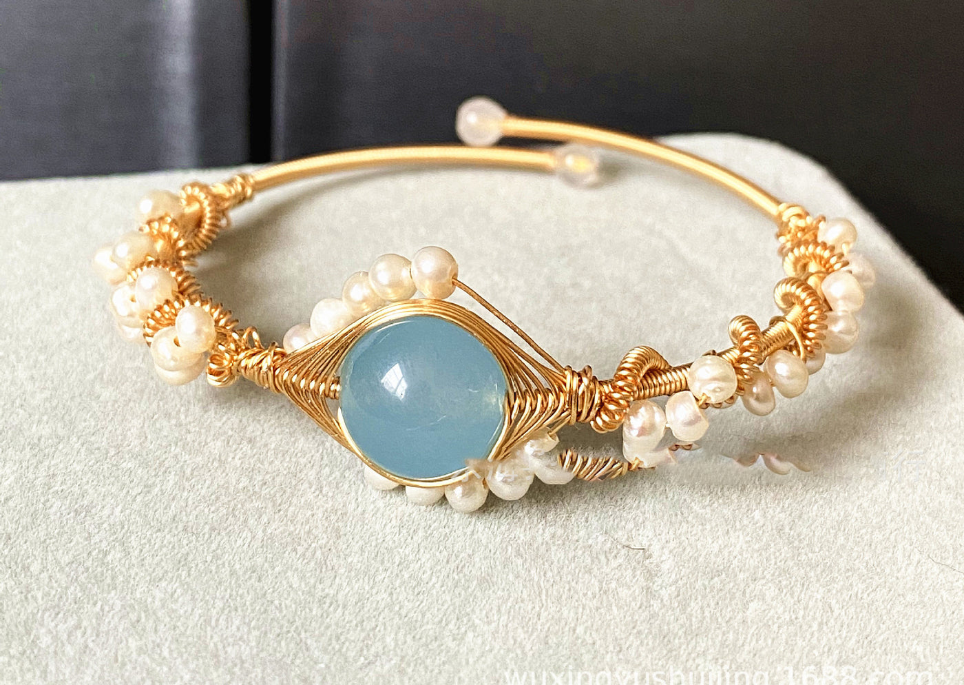 front view of Gold bracelet with pearls and a blue stone on a white surface