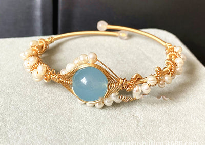 front view of Gold bracelet with pearls and a blue stone on a white surface