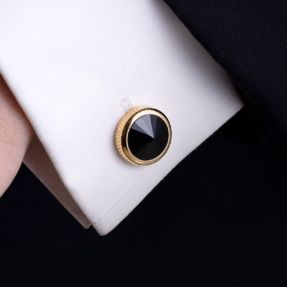 Gold and black cufflink on a white cuff against a dark background
