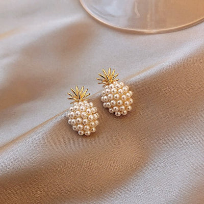 Pineapple-shaped earrings with pearl details on a beige fabric background