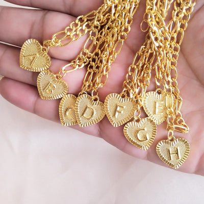 Gold anklets with heart-shaped letter charms held in a hand.