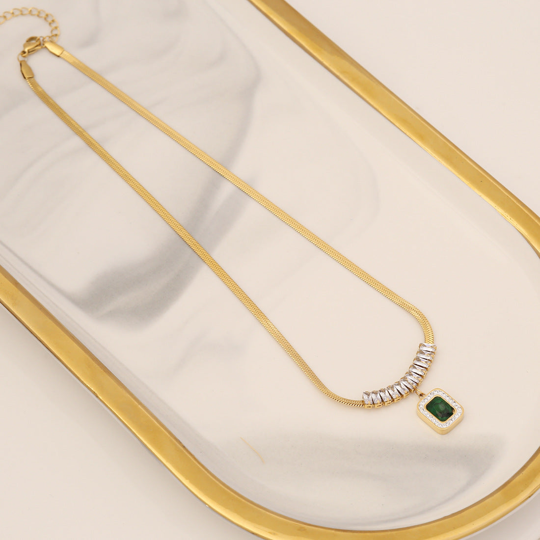 Gold necklace with a green gemstone on a white surface