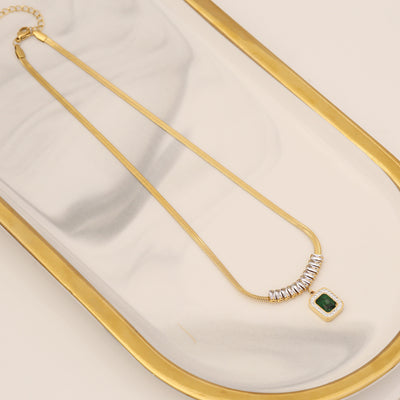 Gold necklace with a green gemstone on a white surface