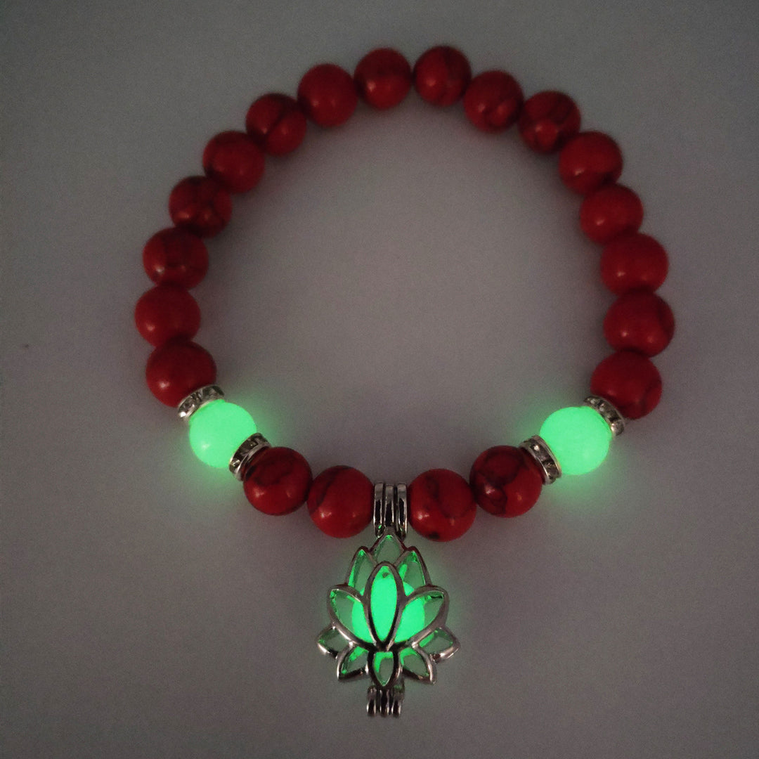 Bracelet with red beads and a glowing green lotus charm on a light gray background