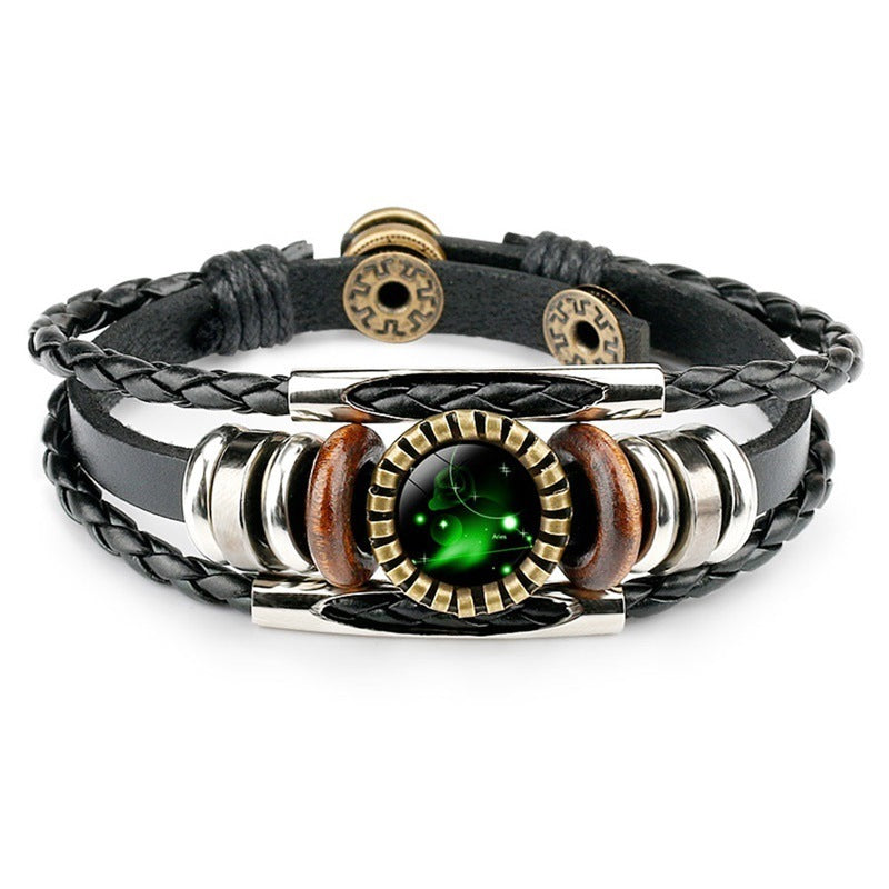 Braided black leather bracelet with metallic and wooden beads, featuring a central circular green emblem with a glowing, mystical design.