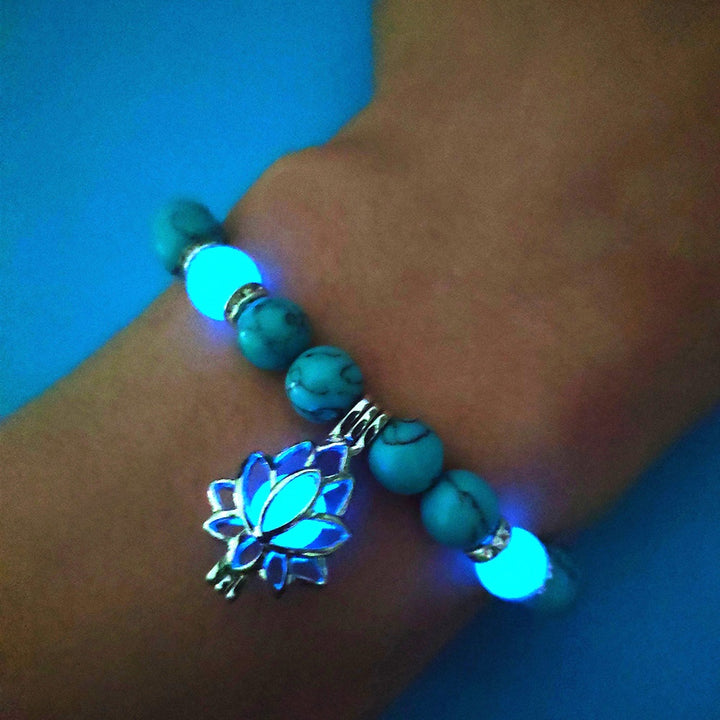 Turquoise beaded bracelet with a glowing blue lotus flower charm on a wrist against a blue background.