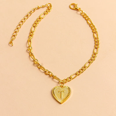Gold chain bracelet with a heart-shaped pendant featuring letter T on a beige background
